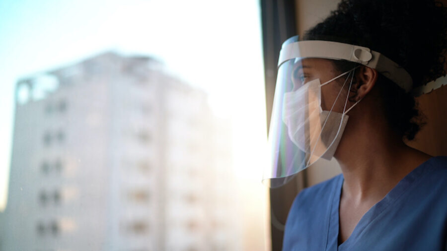 Nurse with protective face mask looking through window at hospital