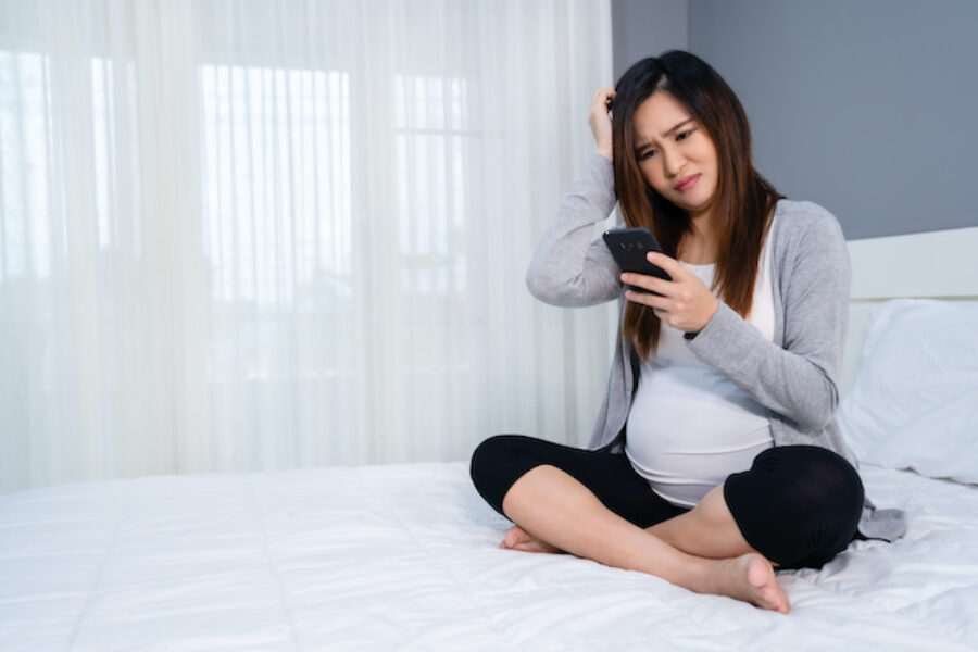 stressed pregnant woman using a smartphone in bed