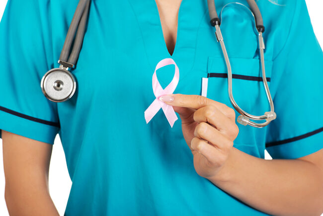 Smiling nurse holding pink breast cancer awareness ribbon.